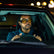 Man driving a car at night with city lights in the background