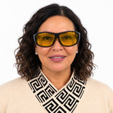 A woman with dark curly hair wearing black-framed safety glasses with yellow lenses.