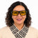 A woman with dark curly hair wearing black-framed safety glasses with yellow lenses.