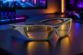 White sports sunglasses with yellow-tinted lenses resting on a dark desk in a gaming setup with a keyboard and monitor in the background.
